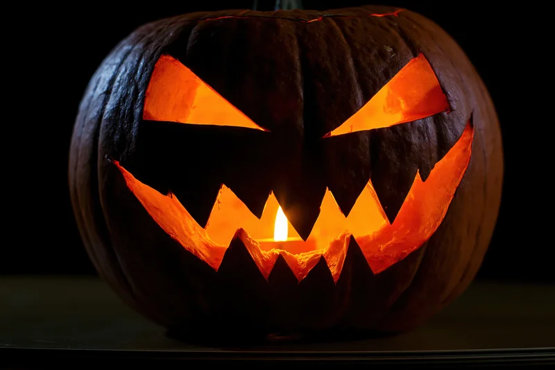 Carved pumpkin with jagged grin lit from within on dark surface