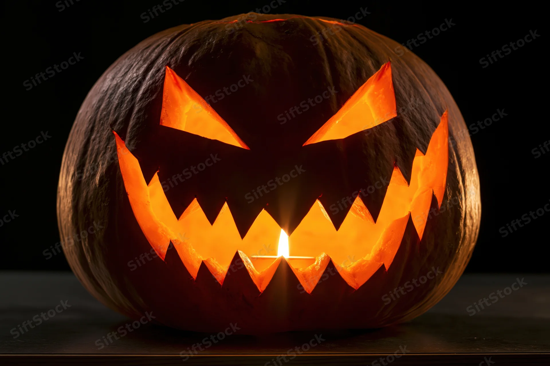 Carved pumpkin with jagged grin lit by candle on dark surface