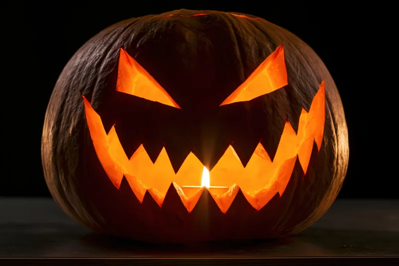 Carved pumpkin with jagged grin lit by candle on dark surface