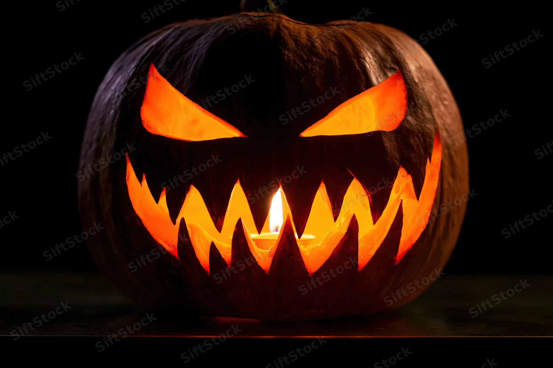 Carved pumpkin with jagged grin lit by candle on dark surface