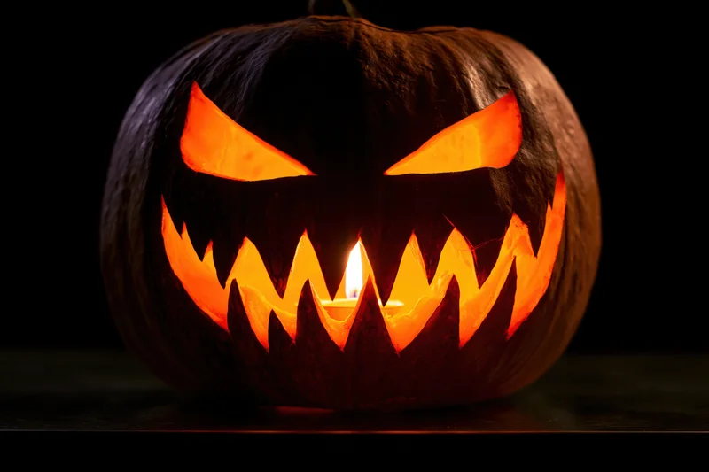 Carved pumpkin with jagged grin lit by candle on dark surface