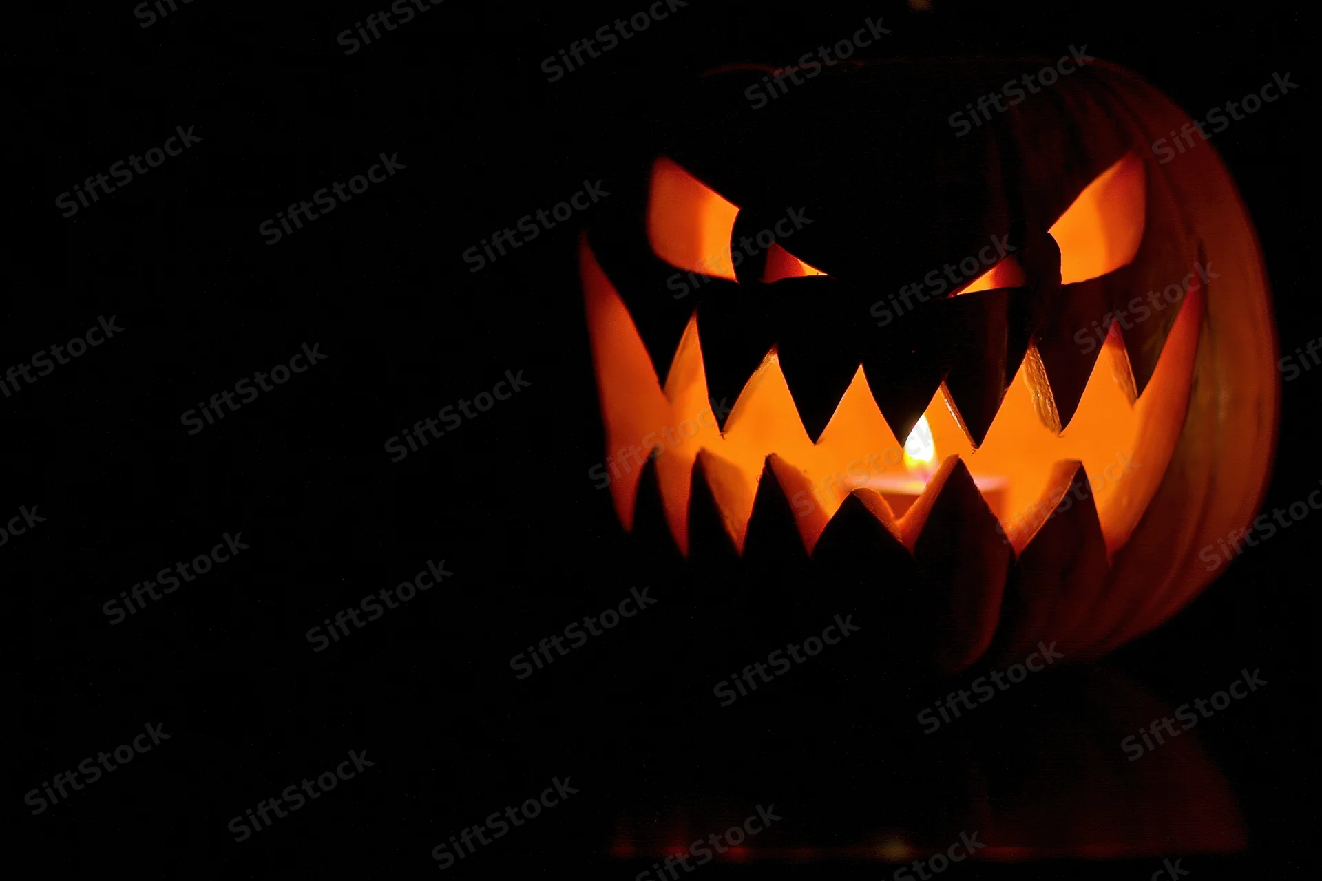 Carved pumpkin with jagged grin lit by candle in dark setting