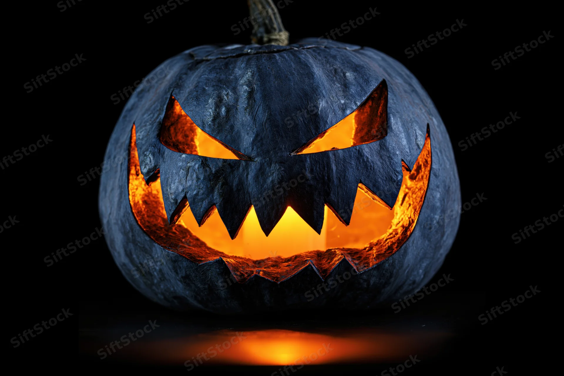 Carved black pumpkin with jagged glowing smile against dark background