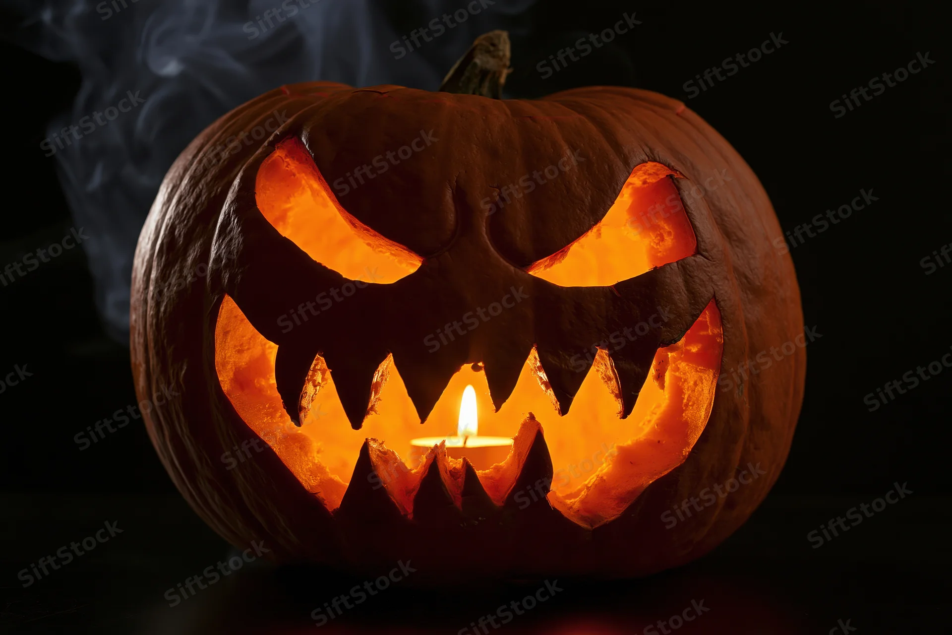 Carved pumpkin with jagged teeth and glowing eyes lit by candle in dark setting
