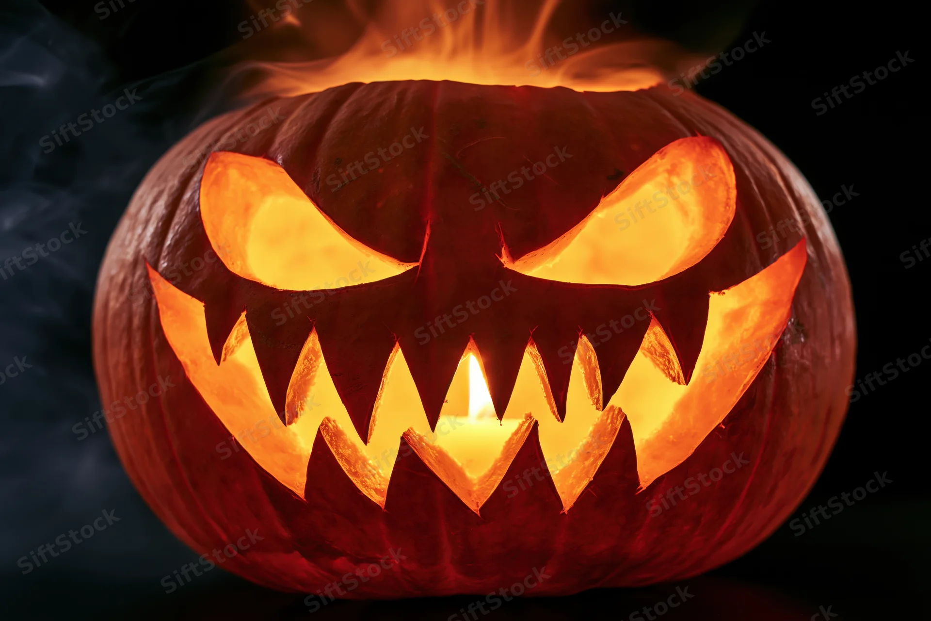Carved pumpkin with jagged teeth and glowing eyes lit by candle in dark smoky setting