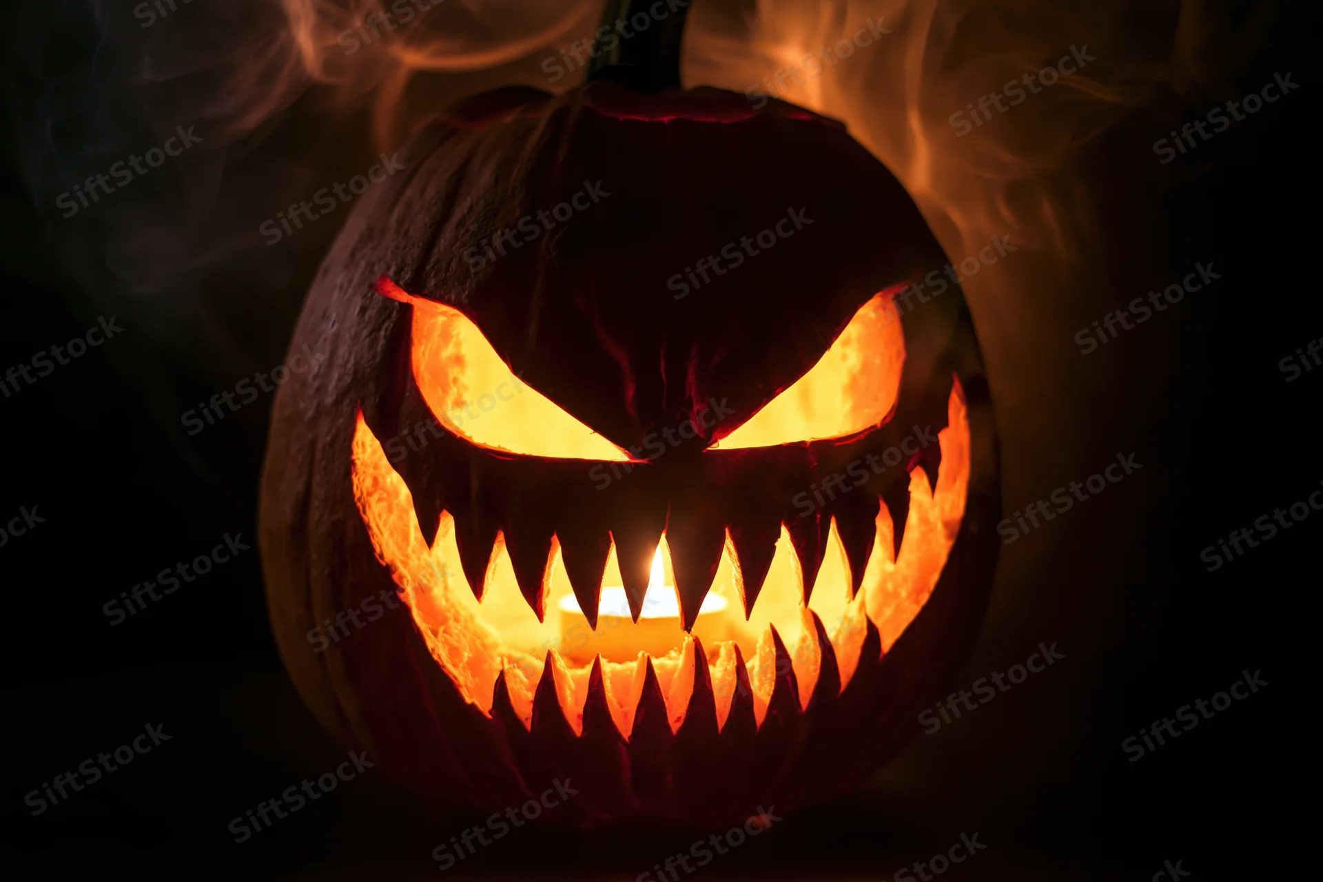 Carved pumpkin with jagged teeth and glowing eyes emitting smoke in dark setting