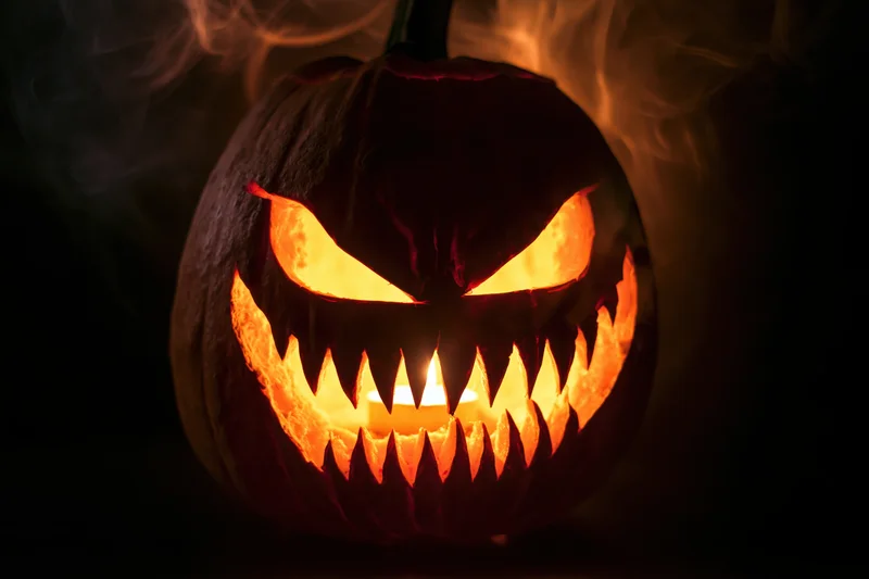 Carved pumpkin with jagged teeth and glowing eyes emitting smoke in dark setting