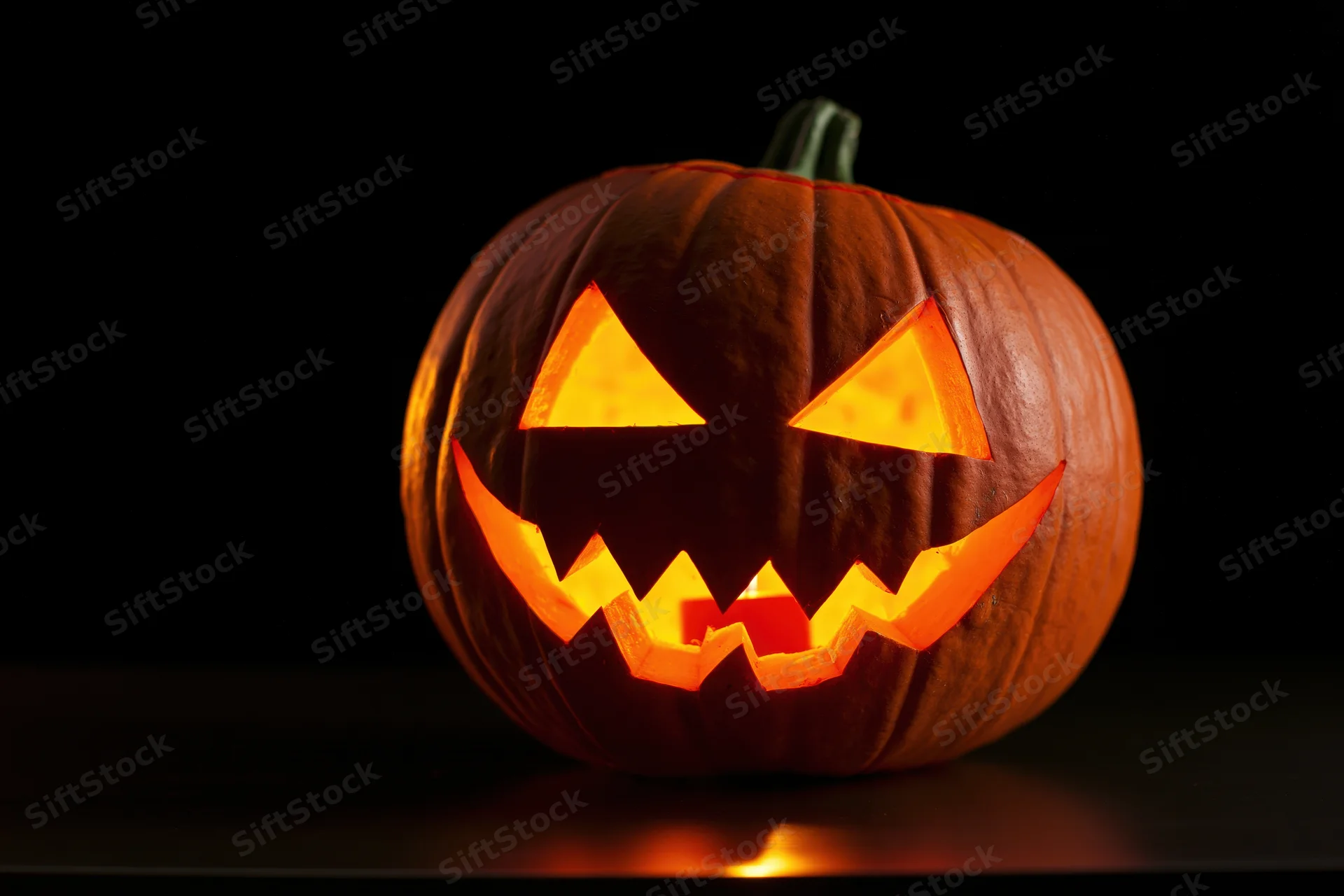 Carved pumpkin with triangle eyes and jagged grin glowing in the dark
