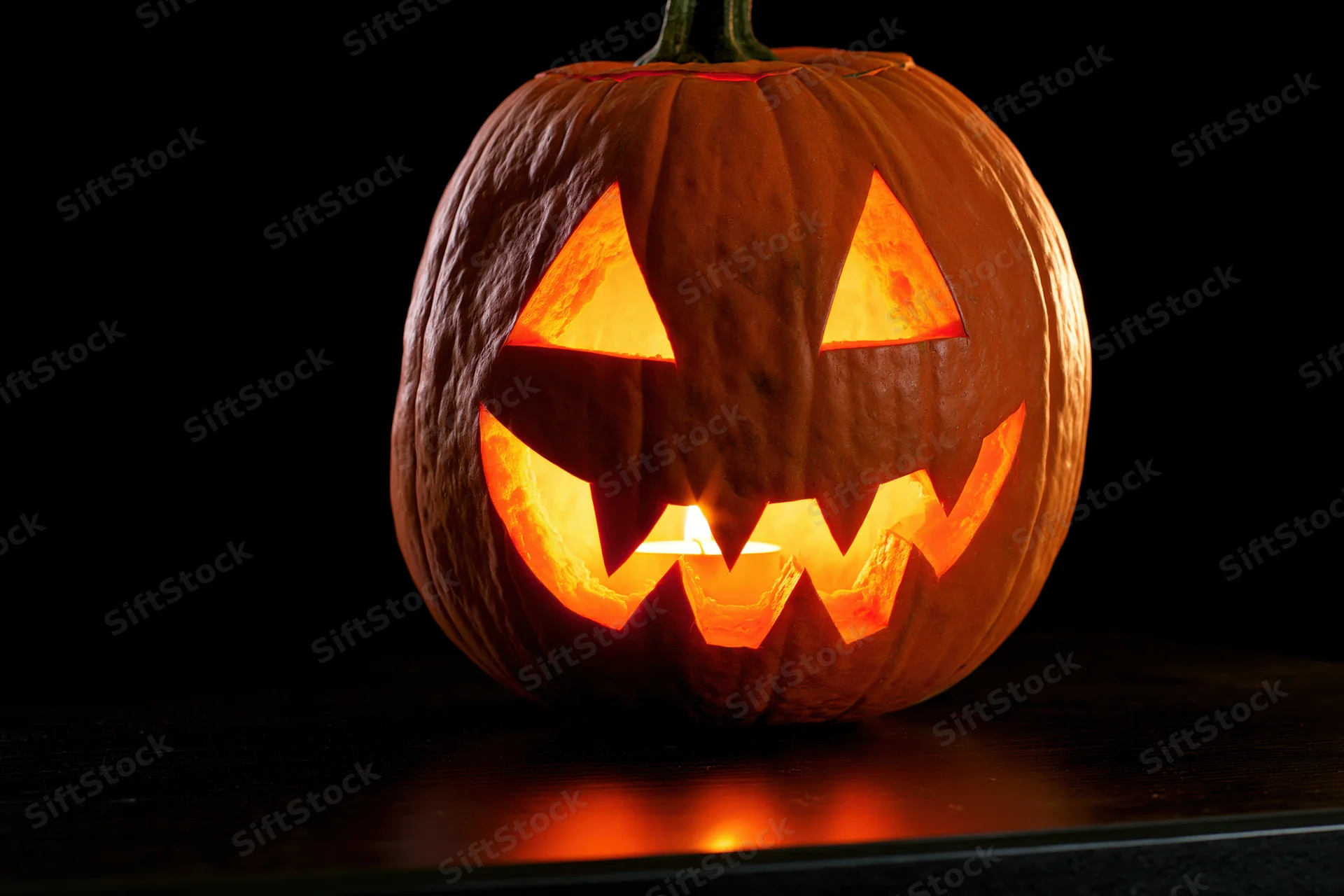 Carved pumpkin with glowing triangular eyes and jagged mouth on dark surface