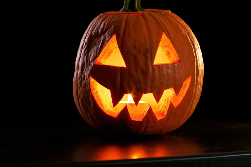 Carved pumpkin with glowing triangular eyes and jagged mouth on dark surface