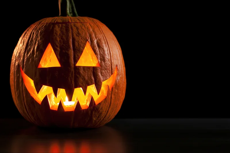 Carved pumpkin with glowing triangular eyes and jagged grin on dark surface