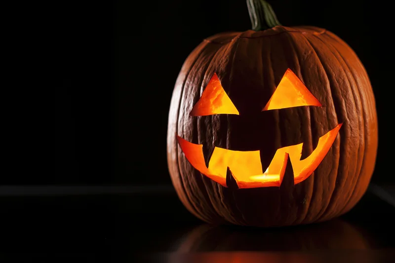 Carved pumpkin with glowing triangular eyes and jagged teeth on dark surface