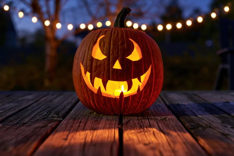 Carved jack-o-lantern glowing with candlelight on wooden table at night outdoors