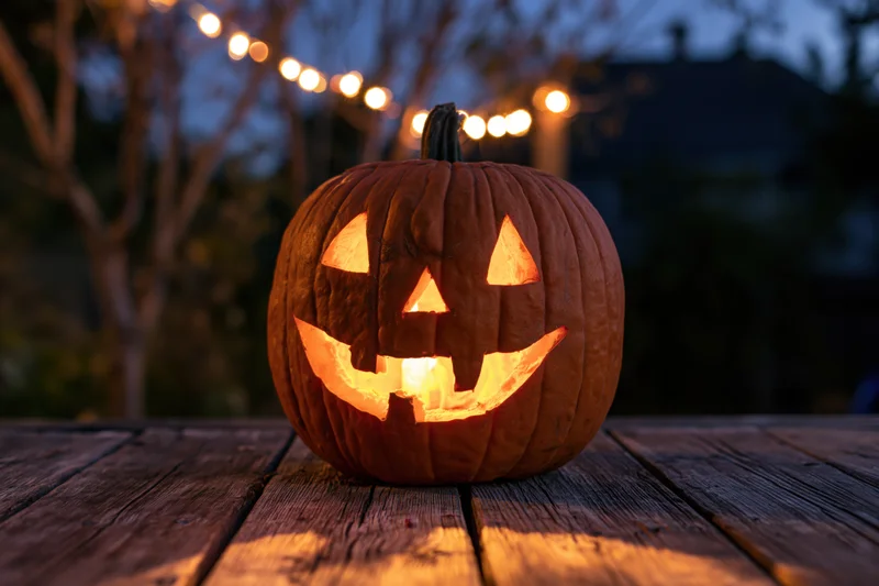 Carved jack-o-lantern glowing from within on a wooden table outdoors at dusk