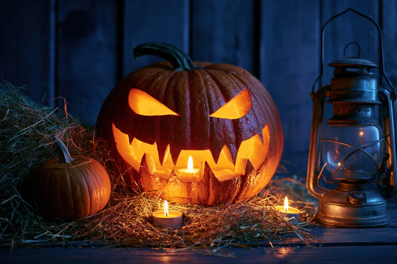 Carved jack-o-lantern glowing with candlelight on hay beside a vintage lantern at night
