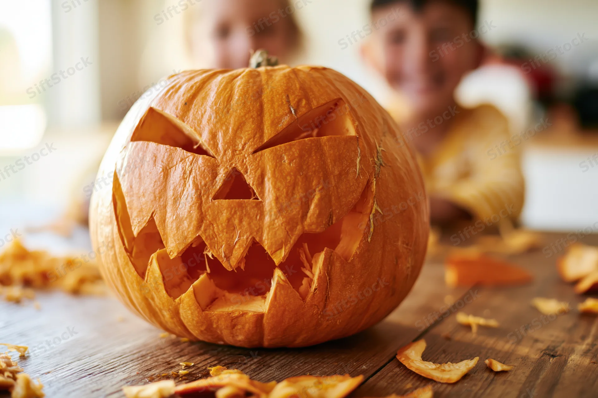 Carved jack-o-lantern with jagged grin on wooden table with children in background
