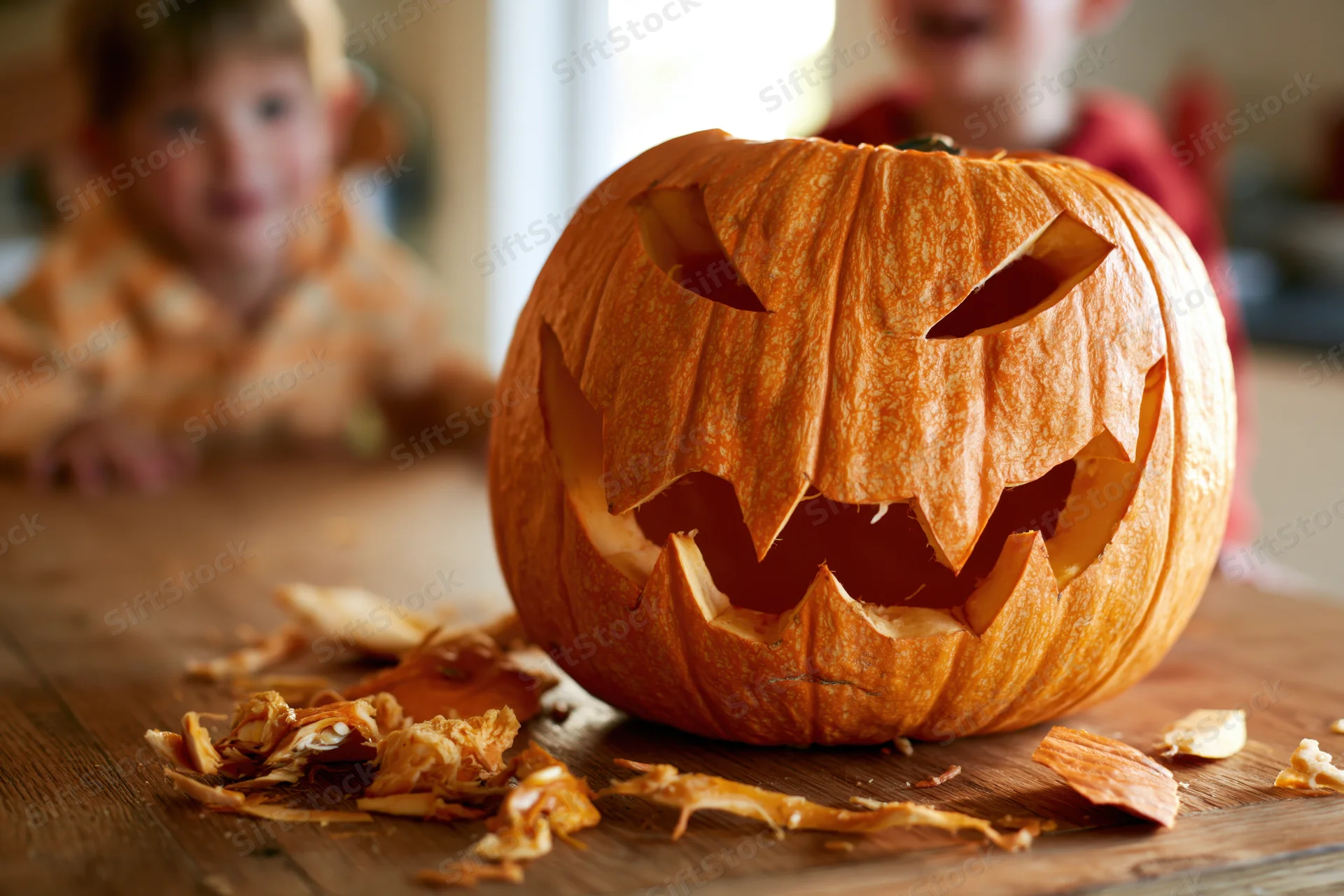 Carved jack-o-lantern with jagged grin on wooden table with children in background