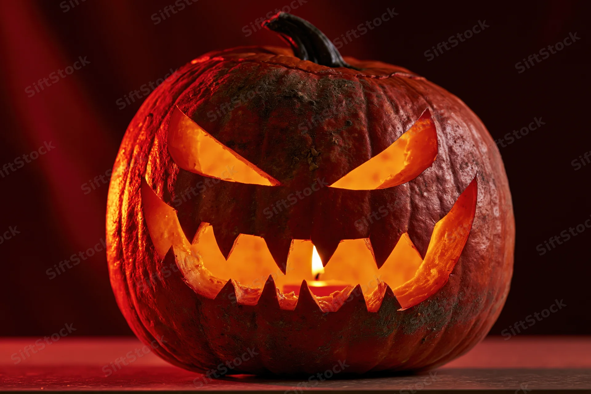 Carved pumpkin with glowing menacing grin lit by candle on dark surface