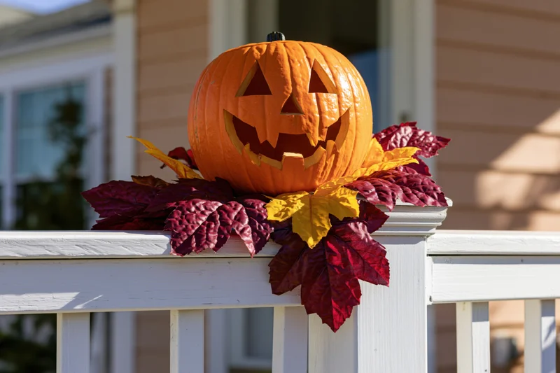 Carved jack-o-lantern with autumn leaves on white porch railing