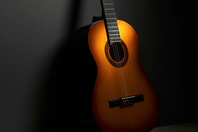 Classical acoustic guitar resting upright against a dark wall, illuminated by spotlight