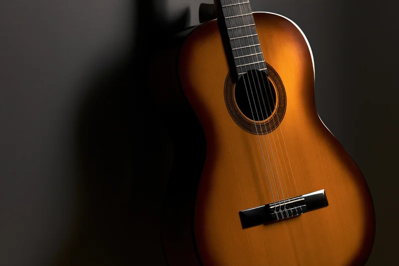 Classical acoustic guitar resting upright against dark background with warm lighting highlighting wood grain and details