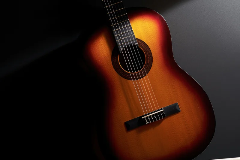 Classical acoustic guitar resting upright against dark background with spotlight highlighting its sunburst wood finish