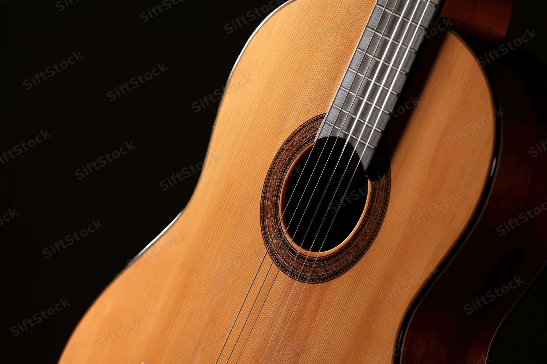 Close-up of a classical acoustic guitar showing wood grain and soundhole against black background