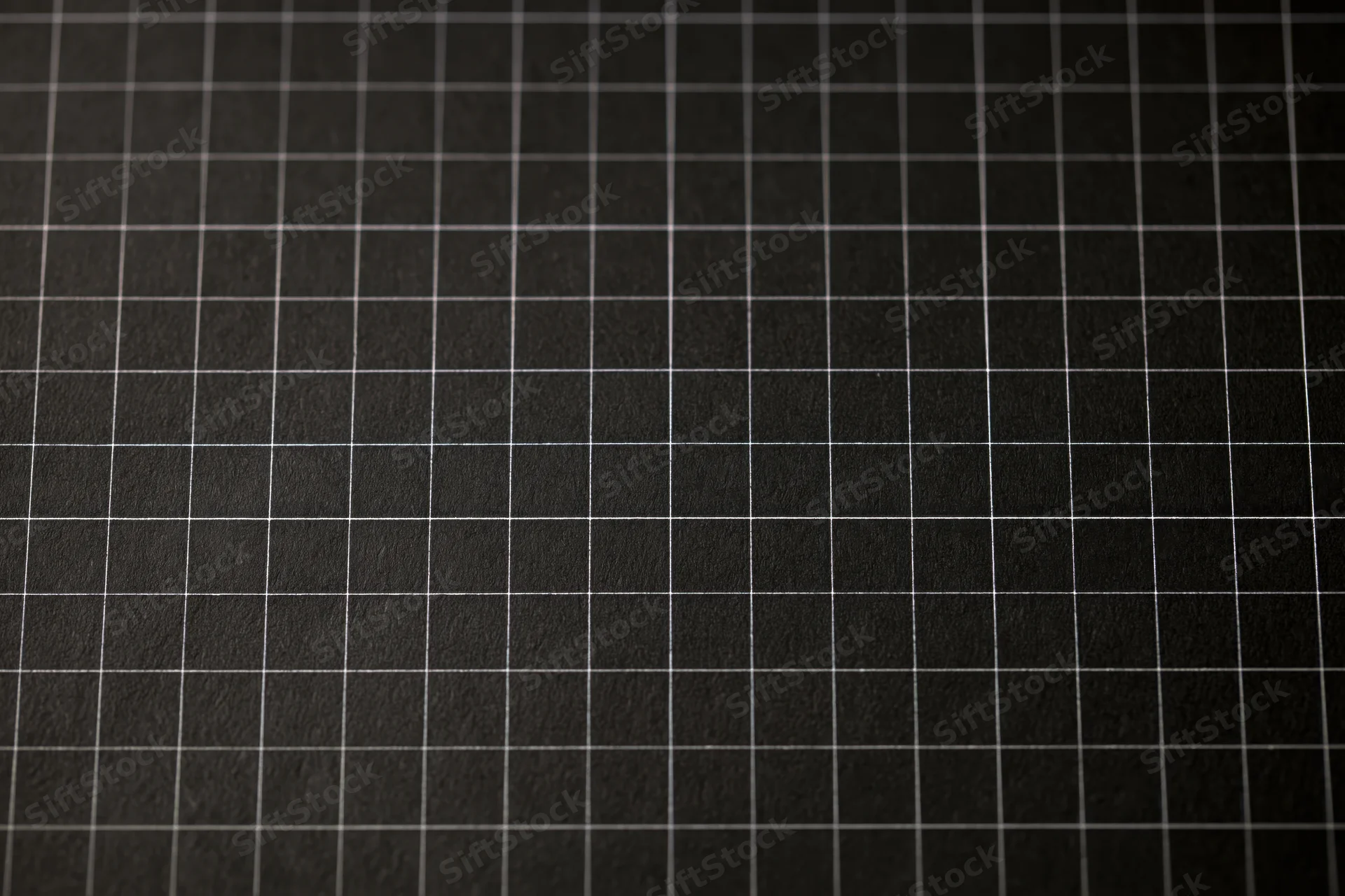 Close-up of dark matte black graph paper with white grid lines covering the surface