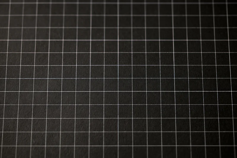Close-up of dark matte black graph paper with white grid lines covering the surface