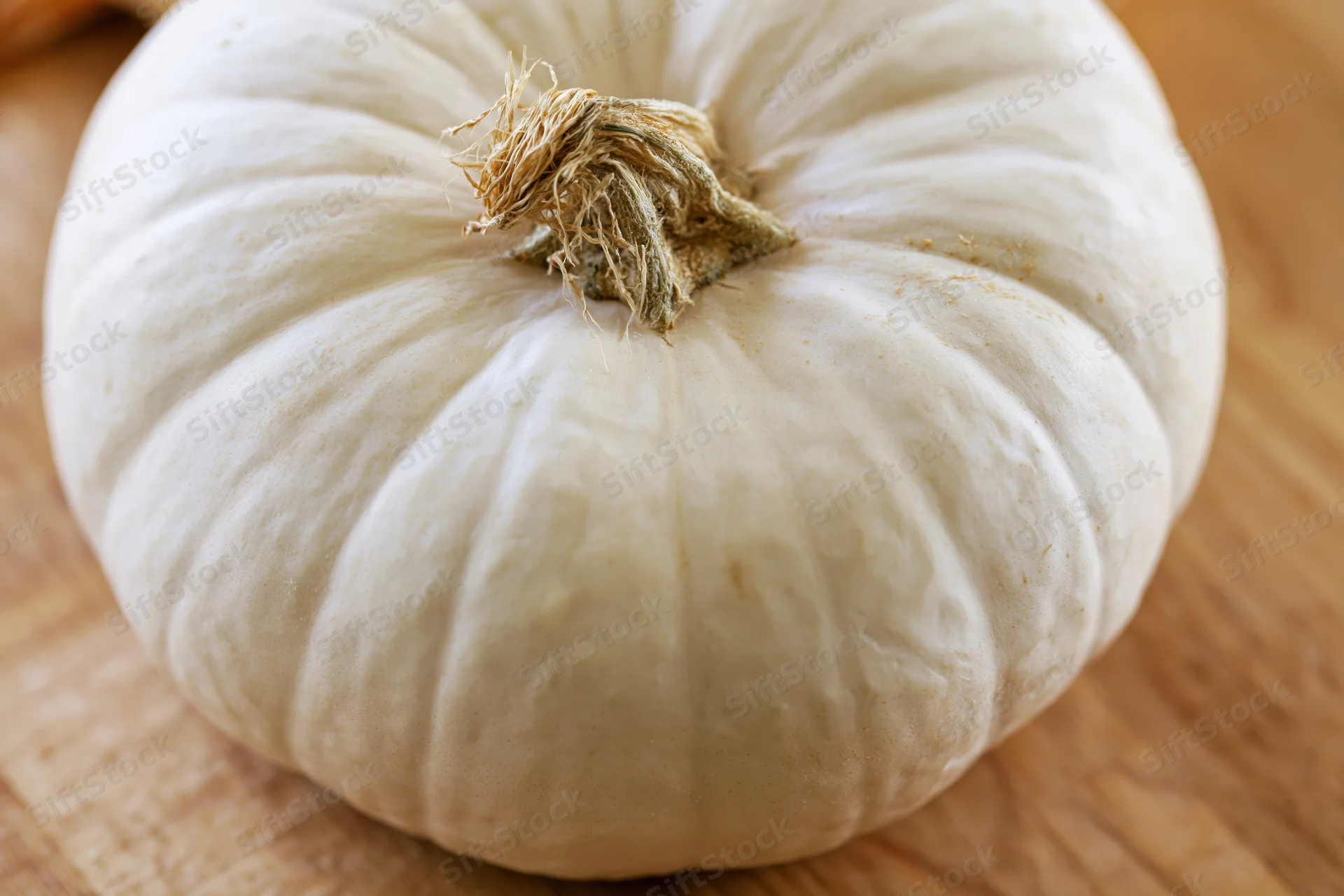 White pumpkin resting on light wooden surface