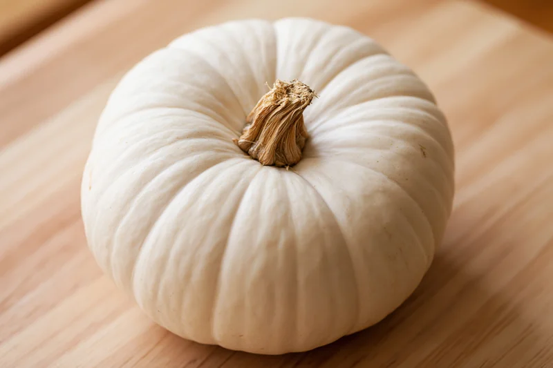 White pumpkin resting on a wooden cutting board