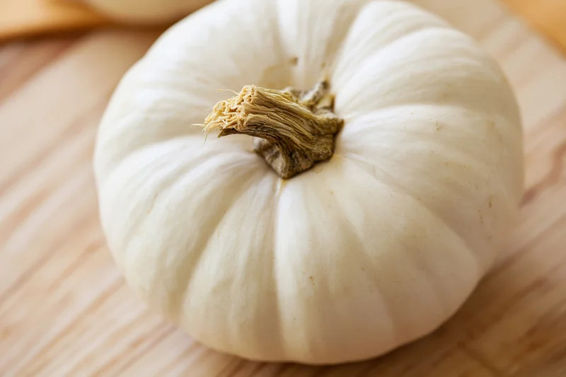 White pumpkin resting on a wooden cutting board