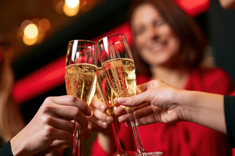 Hands clinking champagne flutes together at a festive indoor party