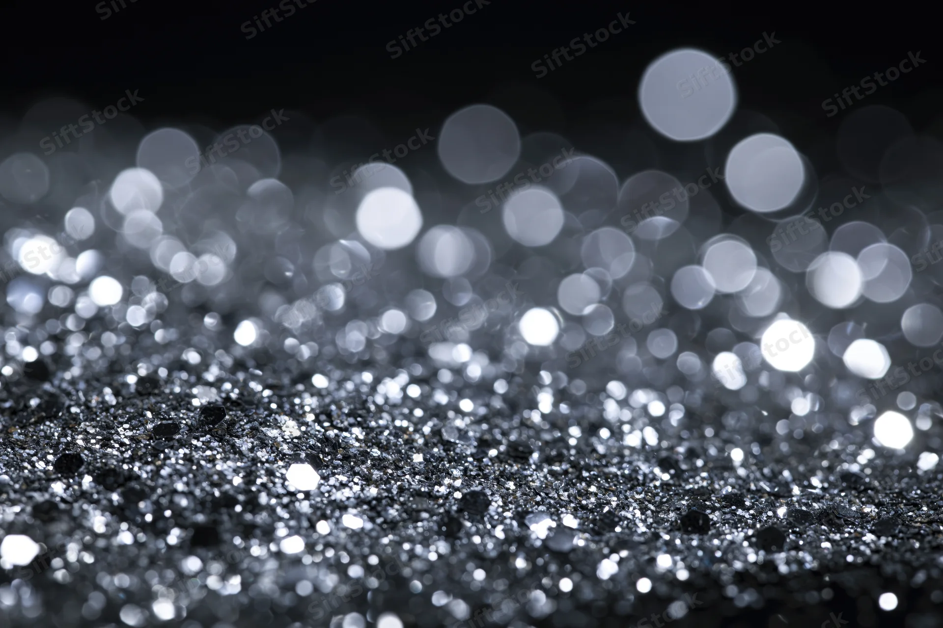 Scattered silver glitter on a flat surface with bokeh lights in the background