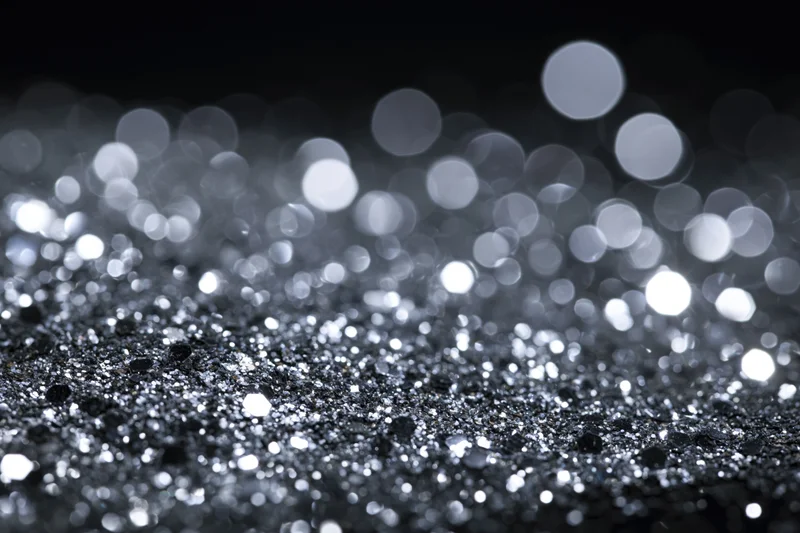 Scattered silver glitter on a flat surface with bokeh lights in the background