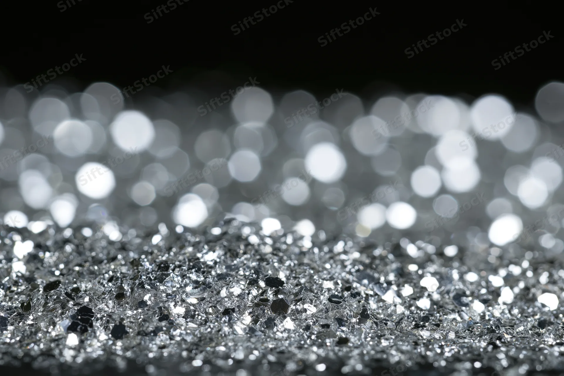 Scattered silver glitter on a flat surface with bokeh background