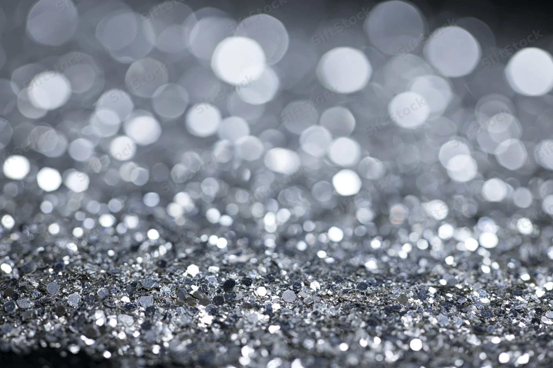 Scattered silver glitter on a flat surface with bokeh highlights in the background