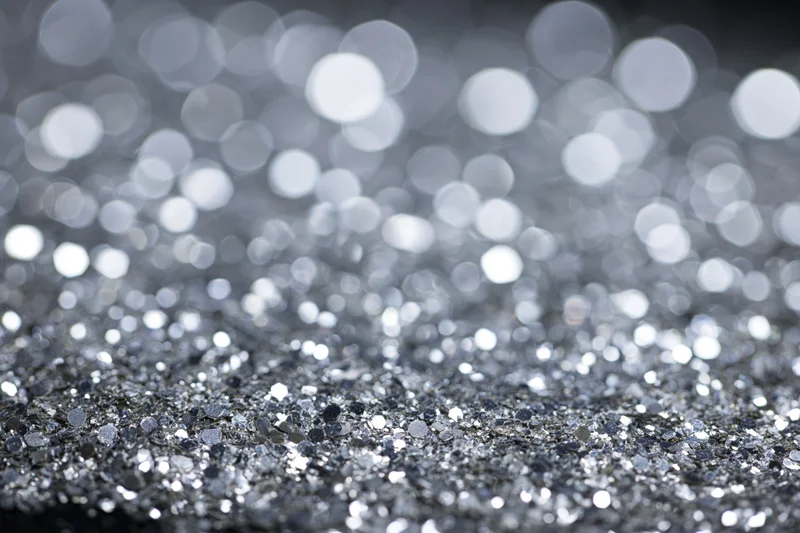 Scattered silver glitter on a flat surface with bokeh highlights in the background