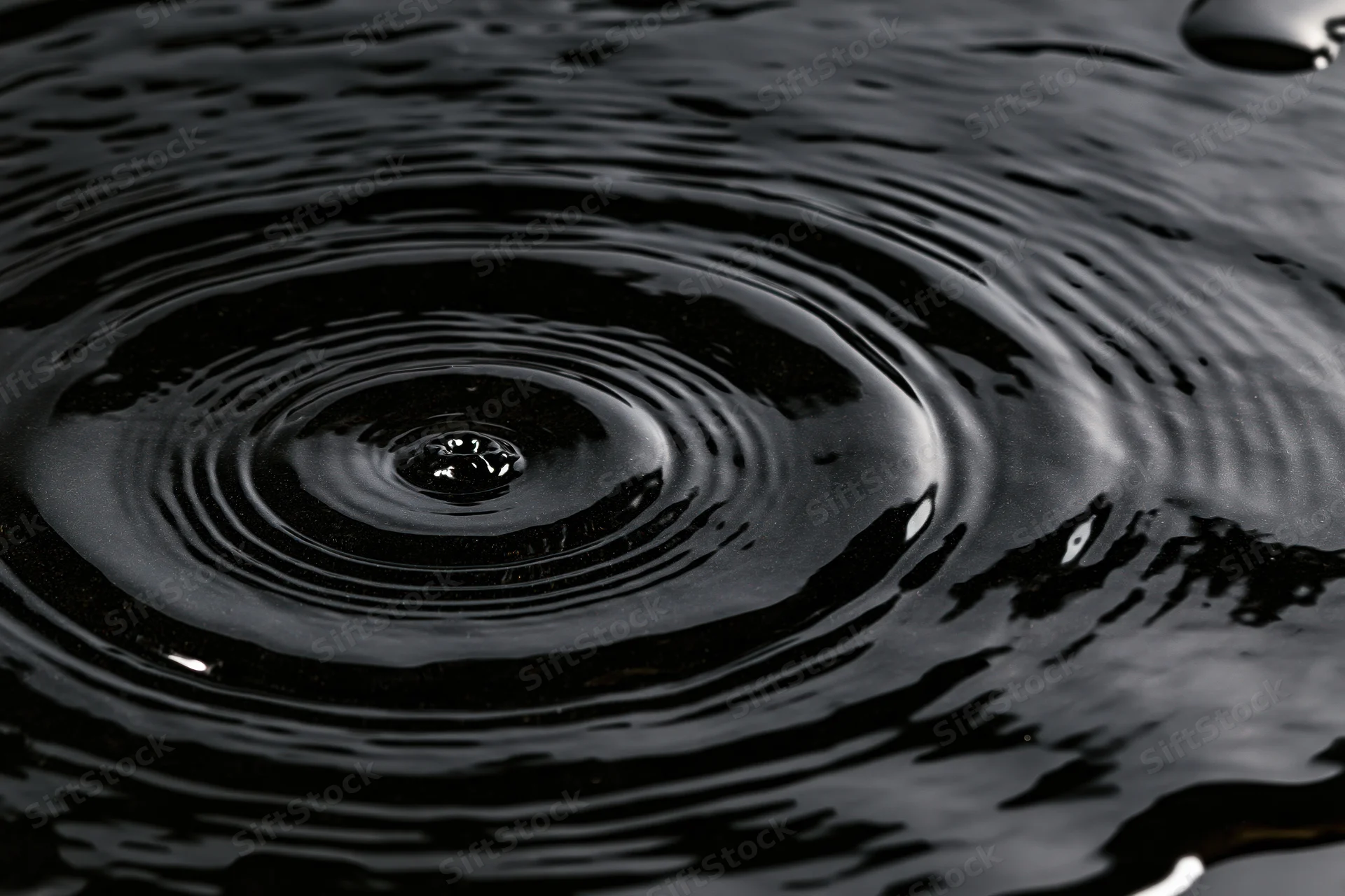 Dark liquid surface with concentric ripples from a falling drop