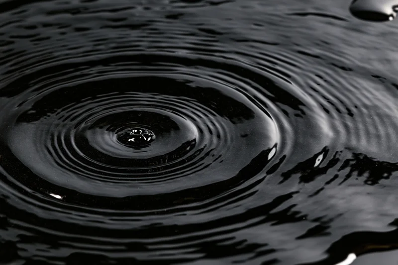 Dark liquid surface with concentric ripples from a falling drop