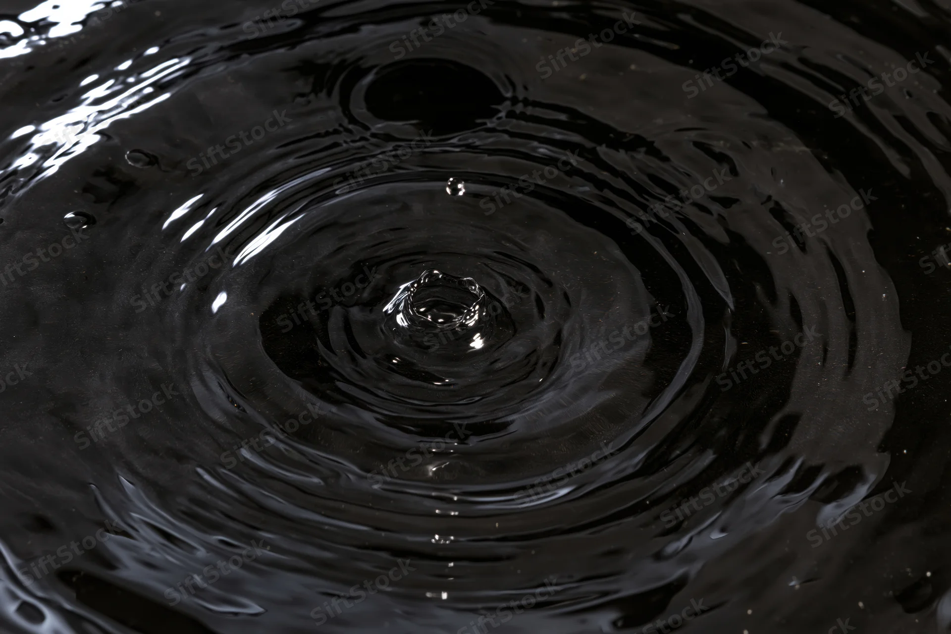 Dark liquid surface with concentric ripples from a droplet impact