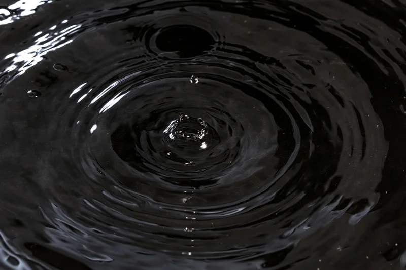 Dark liquid surface with concentric ripples from a droplet impact