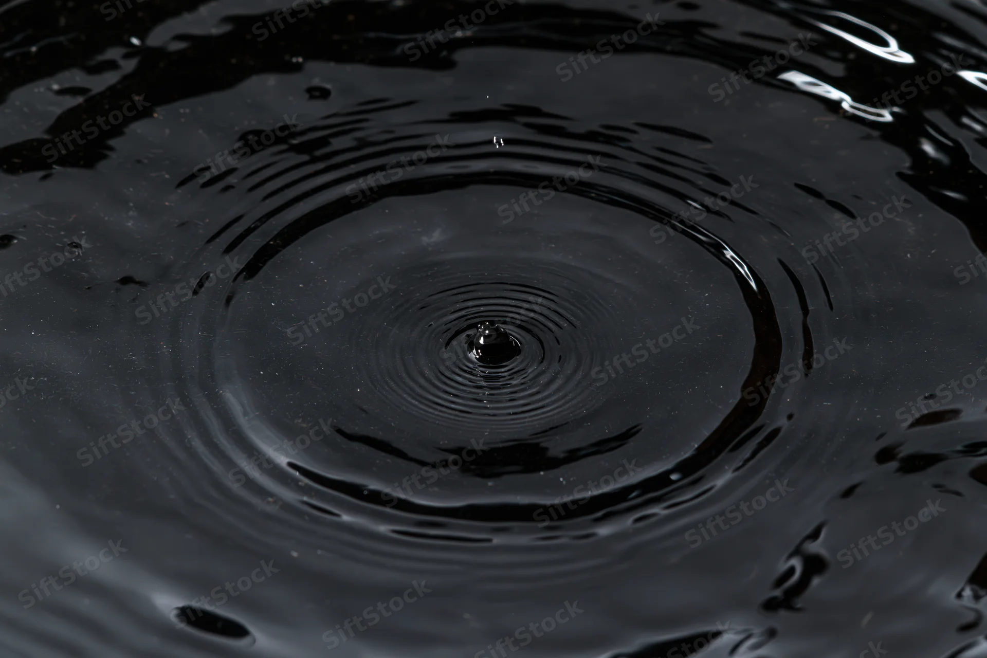 Dark liquid surface with concentric ripples from a falling drop, overhead closeup