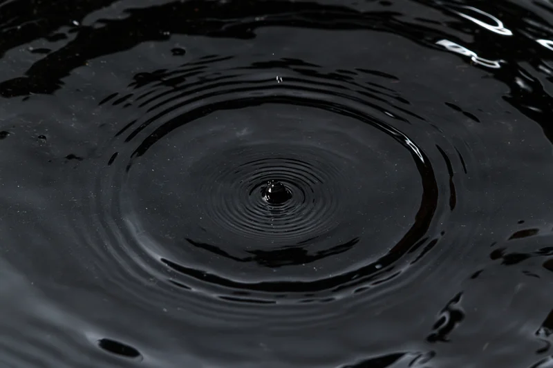 Dark liquid surface with concentric ripples from a falling drop, overhead closeup