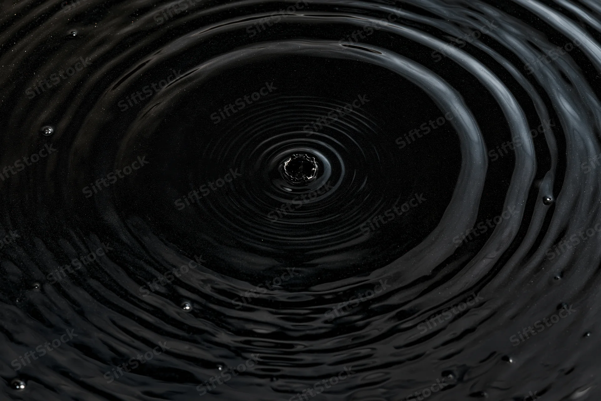 Overhead closeup of dark liquid surface with concentric ripples from a single drop