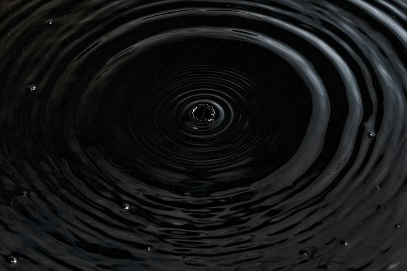 Overhead closeup of dark liquid surface with concentric ripples from a single drop