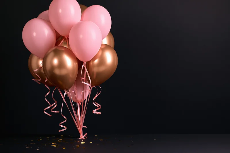 Cluster of pink and metallic gold helium balloons with curling ribbons on dark background