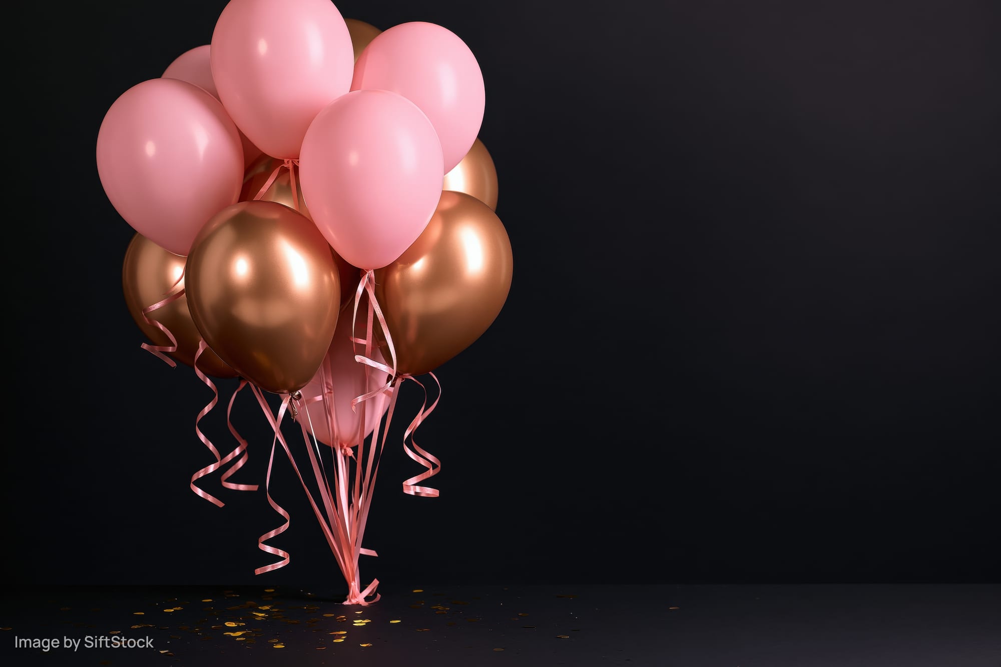 Cluster of pink and metallic gold helium balloons with curling ribbons on dark background