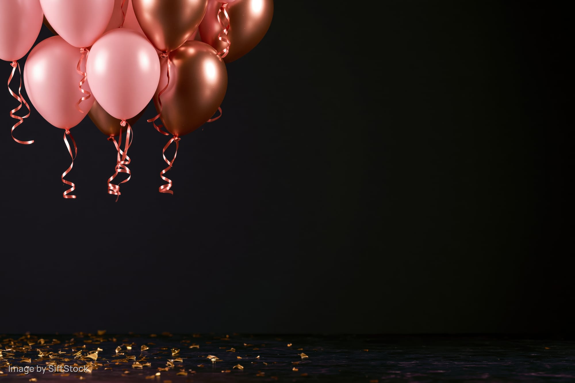 Cluster of pink and metallic gold helium balloons floating above scattered golden confetti on a dark surface