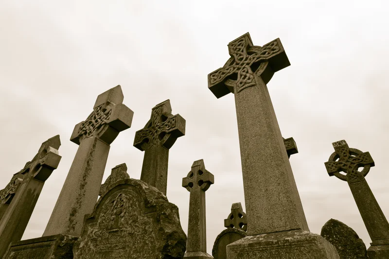Weathered celtic stone crosses standing in a cemetery under an overcast sky